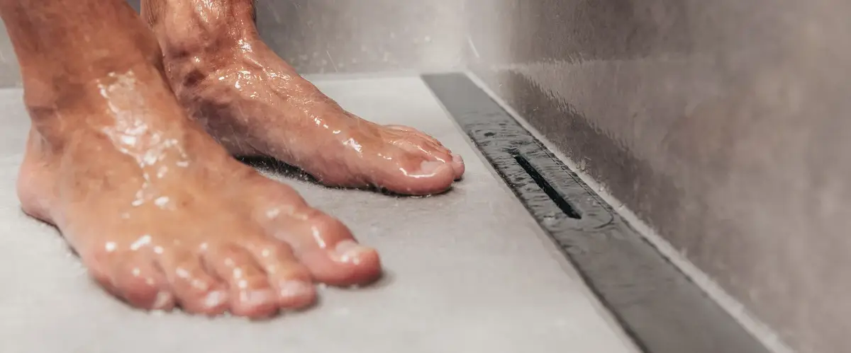 Nasse Füße stehen in einer Dusche neben einem Ablauffliesen.
