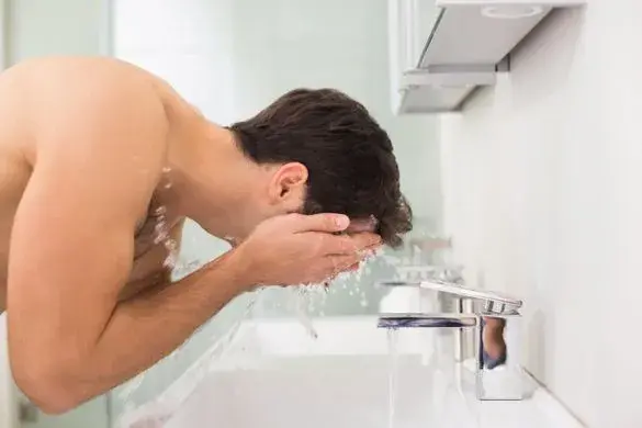 Mann wäscht sich das Gesicht über einem Waschbecken.