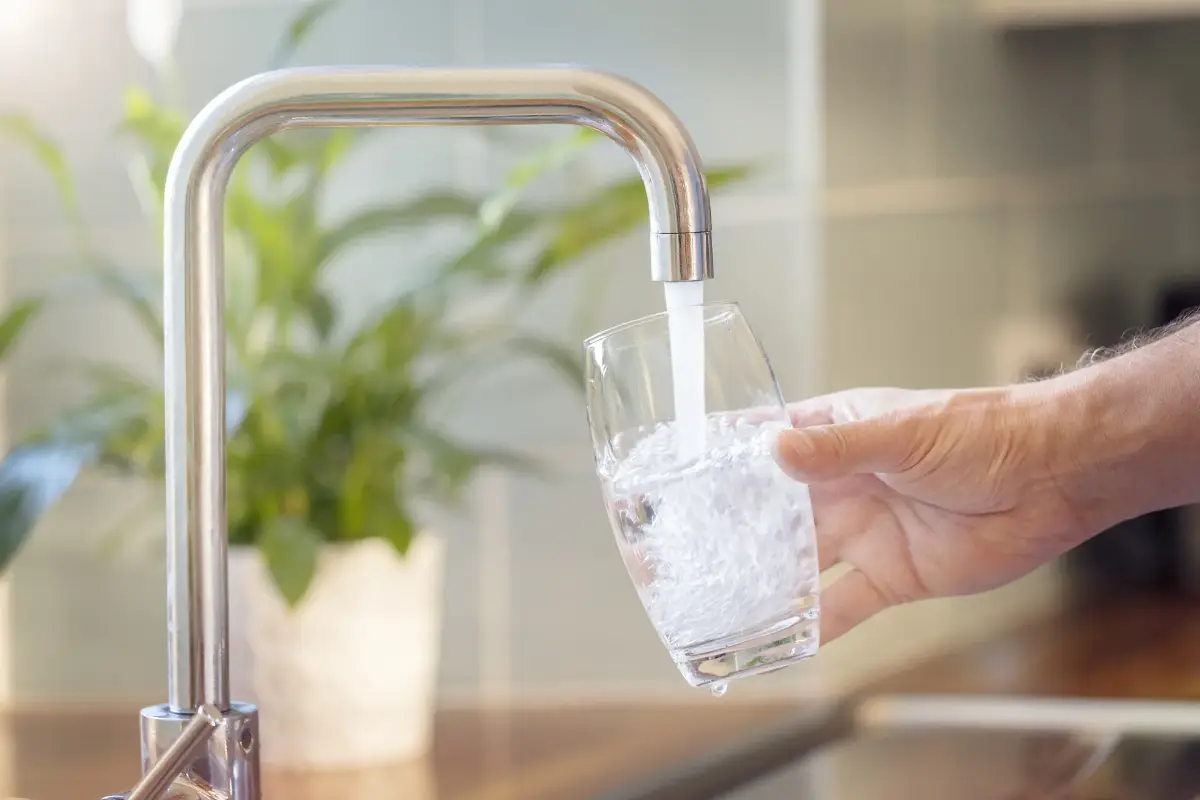 Wasser läuft aus einem Wasserhahn in ein Glas, das eine Hand hält.