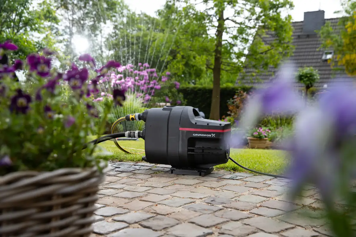 Generator steht auf einem gepflasterten Boden, umgeben von Blumenbeeten.